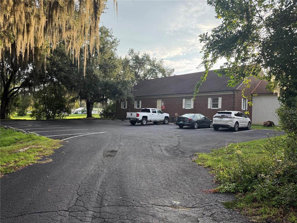 A brick building with a parking lot and three parked vehicles sits under large trees — 500 NE 8TH AVENUE, OCALA, FL