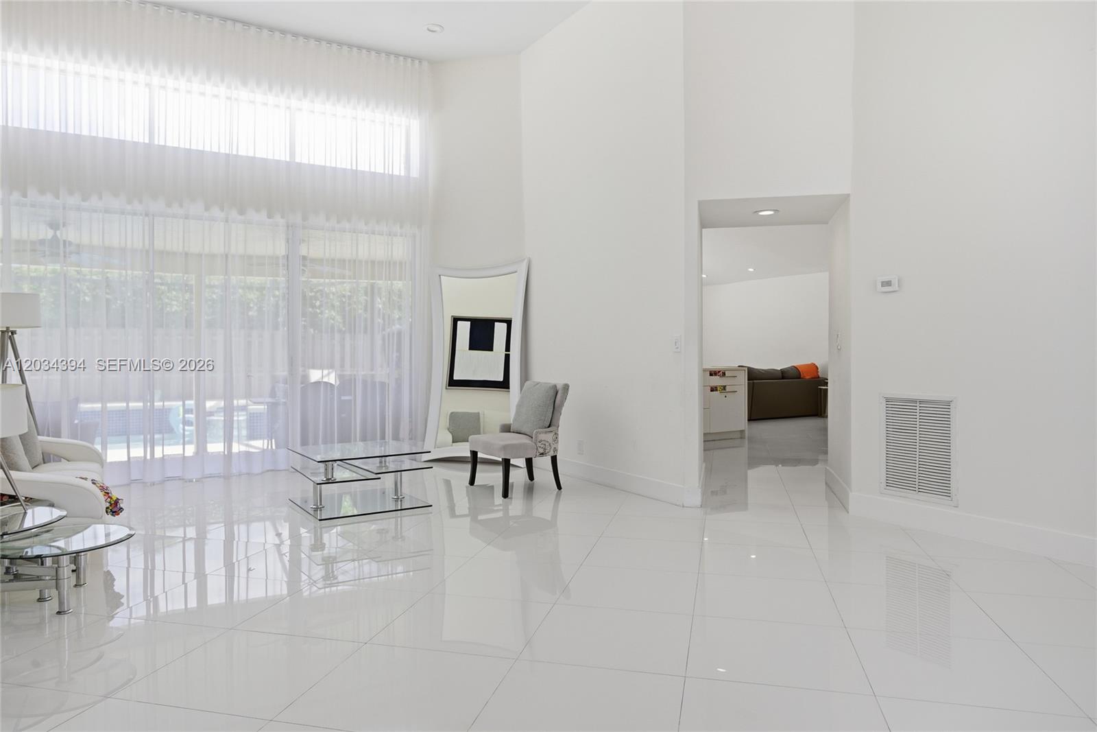 A bright, minimalist living room features white tile floors, high ceilings, and floor-to-ceiling curtains — 9612 N Carousel Cir N, Boca Raton FL 33434, BOCA RATON, FL