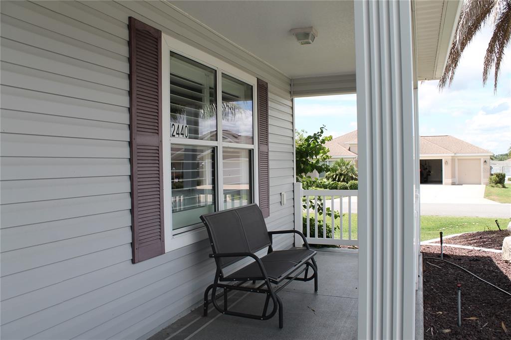 A covered front porch features light gray siding, a dark bench, and white railings — 2440 KATE HILL STREET, THE VILLAGES, FL