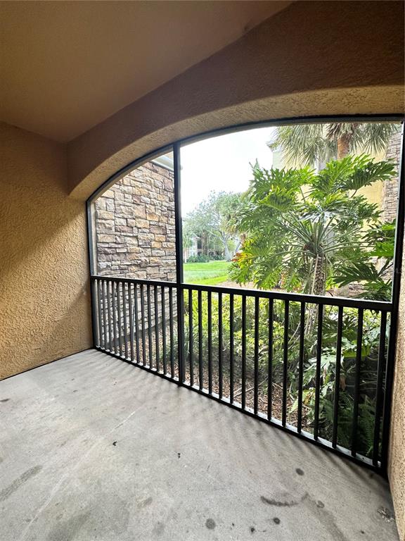 A screened-in balcony features a concrete floor, dark metal railings, and views of lush landscaping — 10023 COURTNEY PALMS BOULEVARD UNIT 101, TAMPA, FL