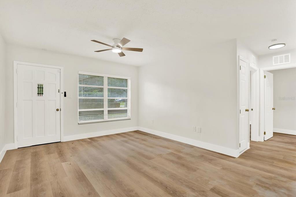 An empty room features light-colored walls, wood-look flooring, a ceiling fan, and a front door — 5543 GULF DRIVE, NEW PORT RICHEY, FL
