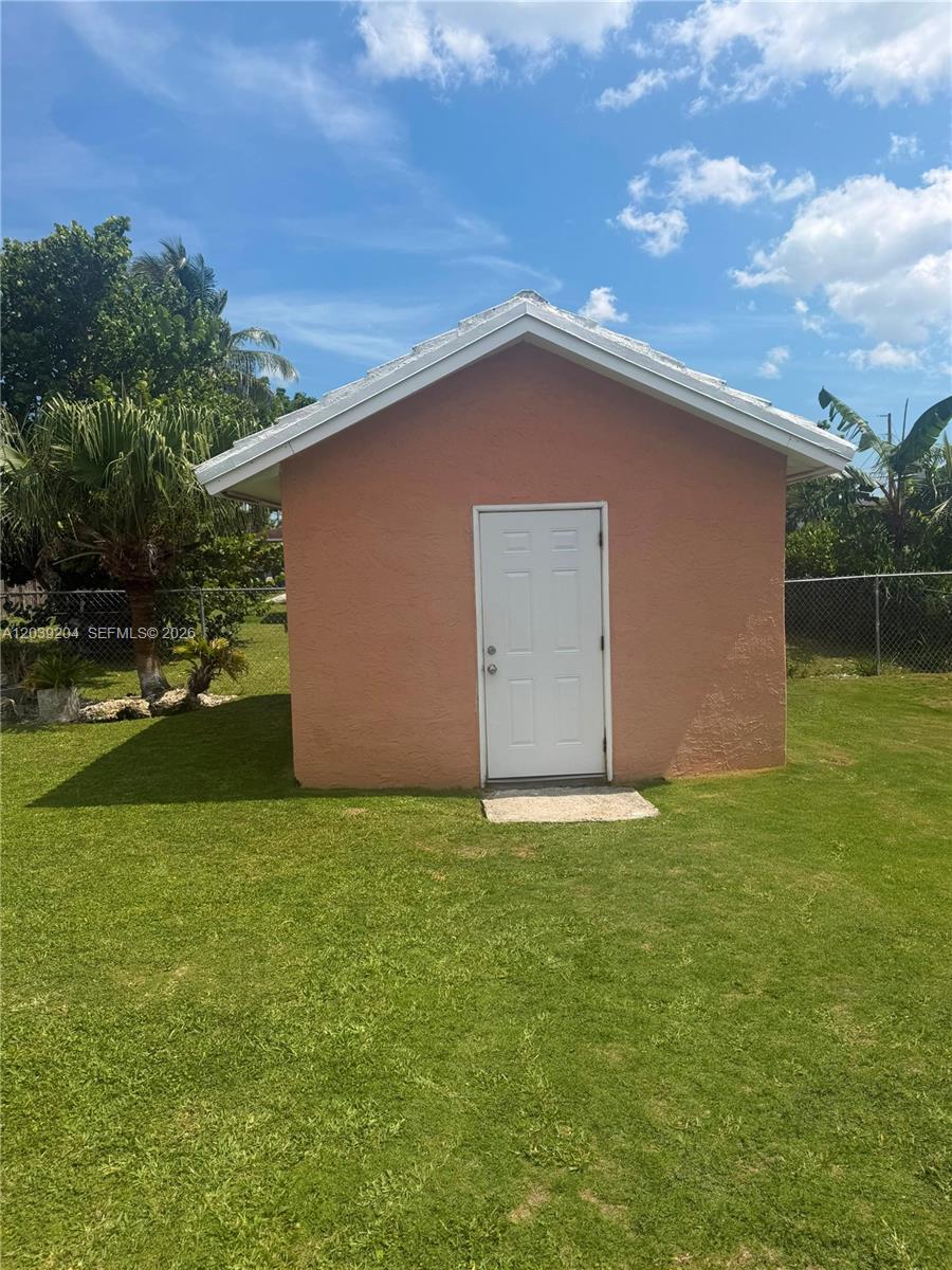 A small, peach-colored detached shed with a white door stands in a grassy yard — 12150 SW 213th Ter, Miami FL 33177, MIAMI, FL