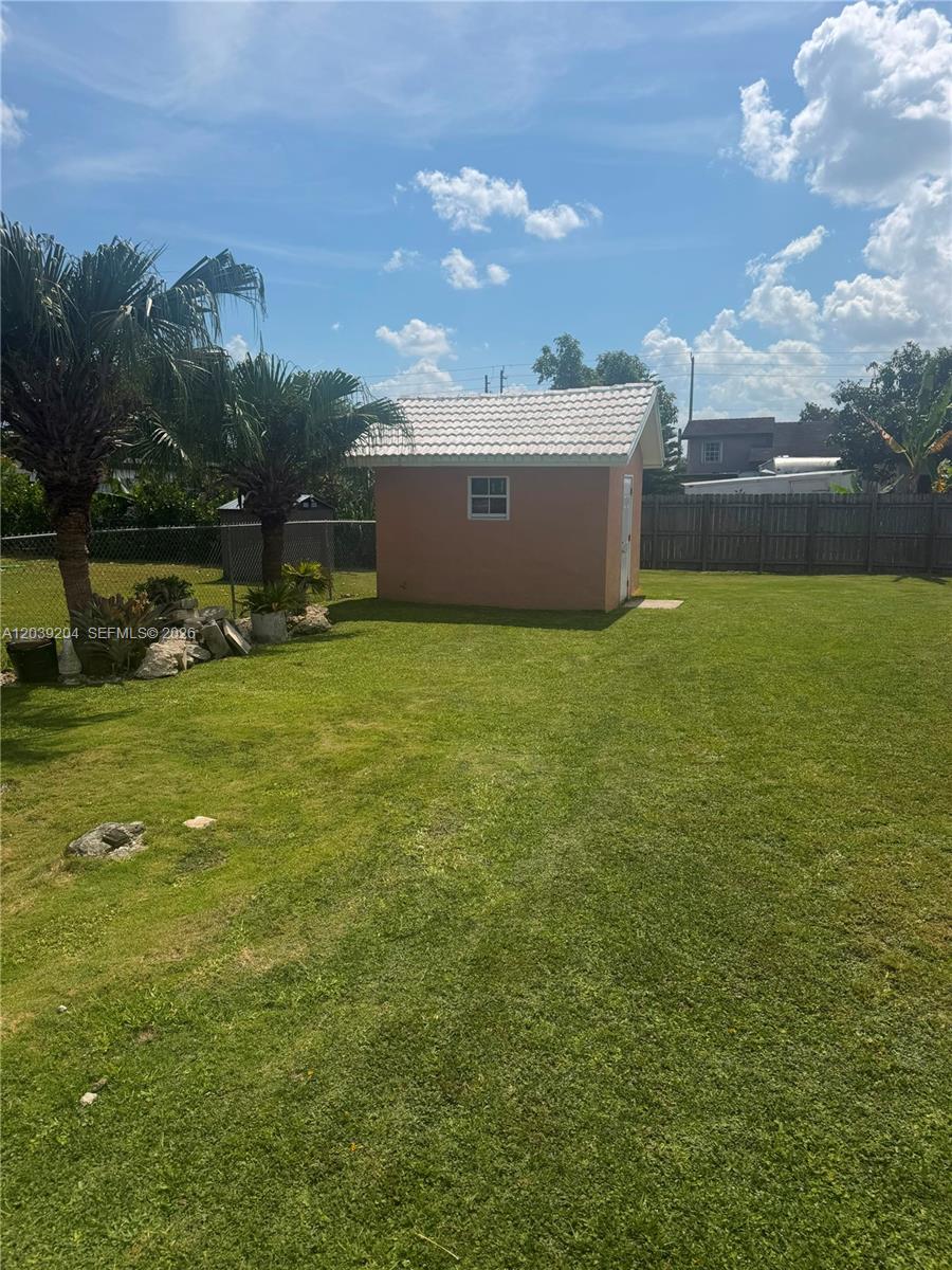 A small, peach-colored shed with a white tiled roof sits in a grassy backyard — 12150 SW 213th Ter, Miami FL 33177, MIAMI, FL