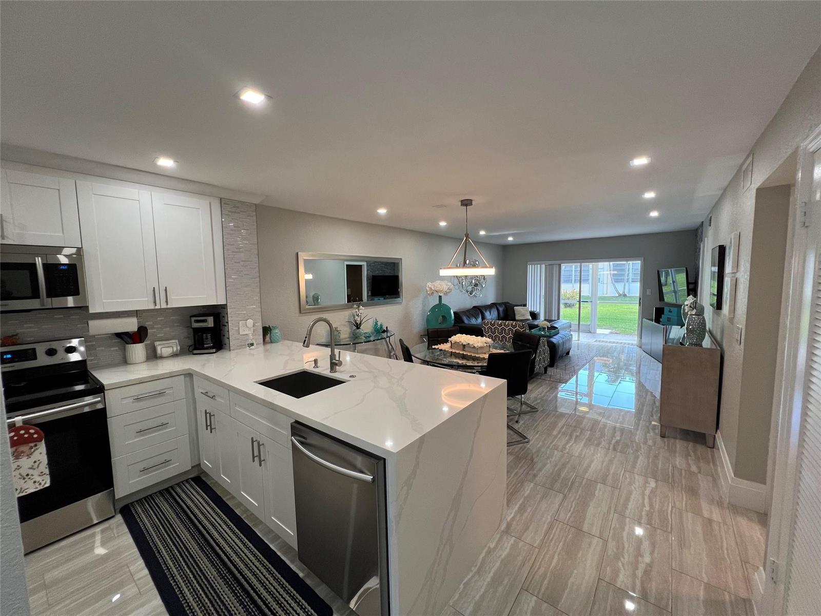 An open-concept kitchen with white cabinets and quartz countertops flows into a living area — 9780 Marina Boulevard # 415, Boca Raton FL 33428, BOCA RATON, FL