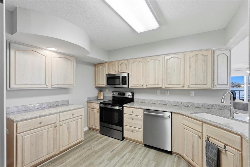 A kitchen features light wood cabinets, granite countertops, stainless steel appliances, and wood-look flooring — 6085 BAHIA DEL MAR CIRCLE UNIT 272, ST PETERSBURG, FL