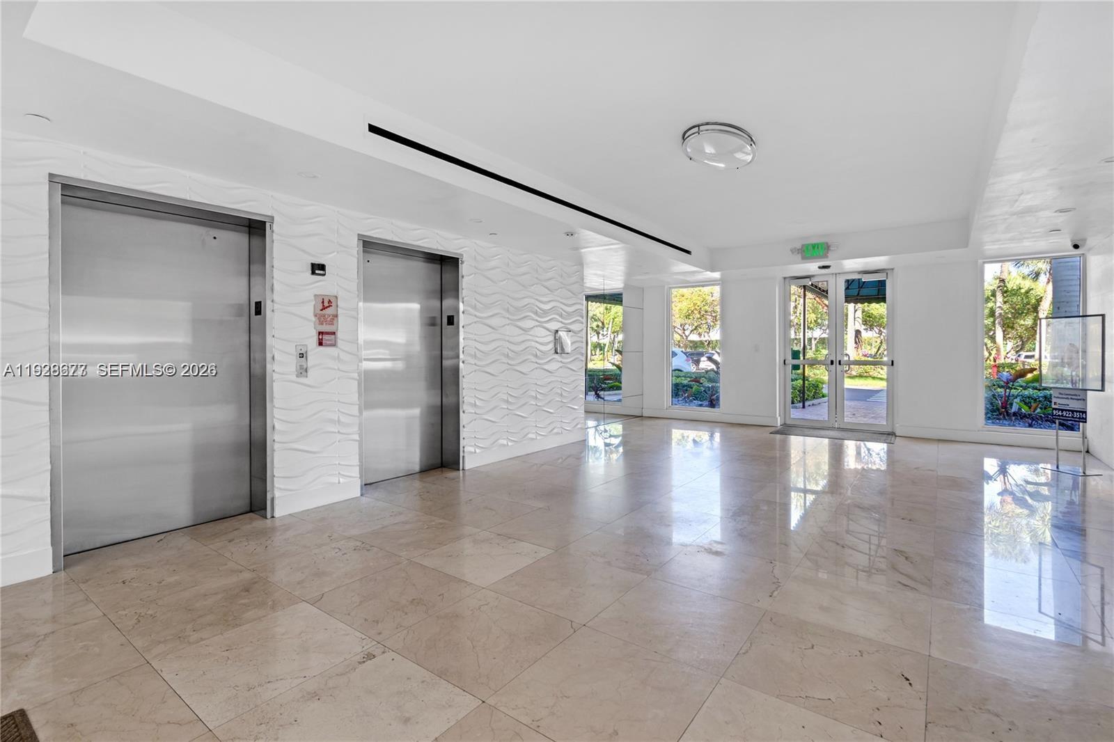 A modern lobby features two stainless steel elevators, textured white walls, and polished tile floors — 10750 NW 66th St # 208, Doral FL 33178, DORAL, FL