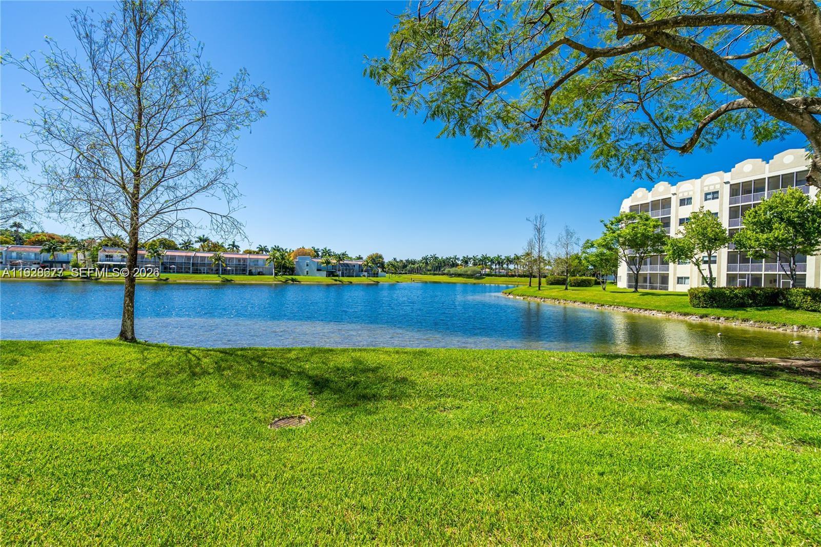 A view of a lake surrounded by green grass, trees, and multi-story apartment buildings — 10750 NW 66th St # 208, Doral FL 33178, DORAL, FL