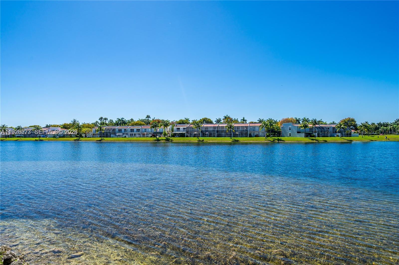 A lake view of a row of multi-story residential buildings under a clear blue sky — 10750 NW 66th St # 208, Doral FL 33178, DORAL, FL
