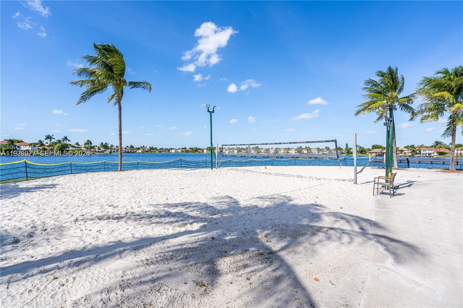 A sandy volleyball court sits beside a lake under a bright blue sky — 10750 NW 66th St # 208, Doral FL 33178, DORAL, FL
