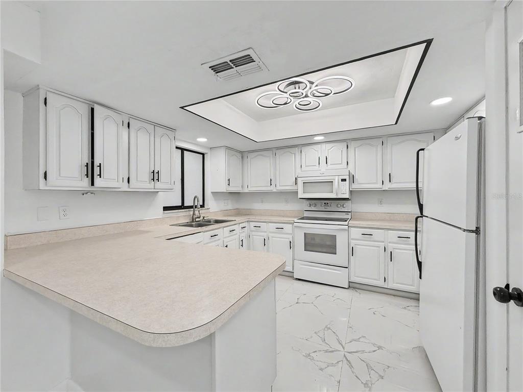 A white kitchen features a peninsula, laminate countertops, white cabinets, and a modern ceiling light — 2101 HIBISCUS ROAD, FORT MYERS, FL