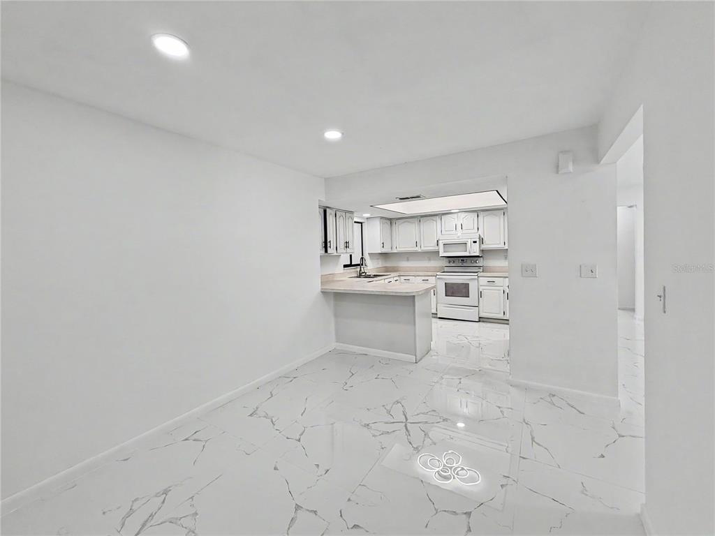 A kitchen with white cabinets and a breakfast bar opens into a dining area — 2101 HIBISCUS ROAD, FORT MYERS, FL