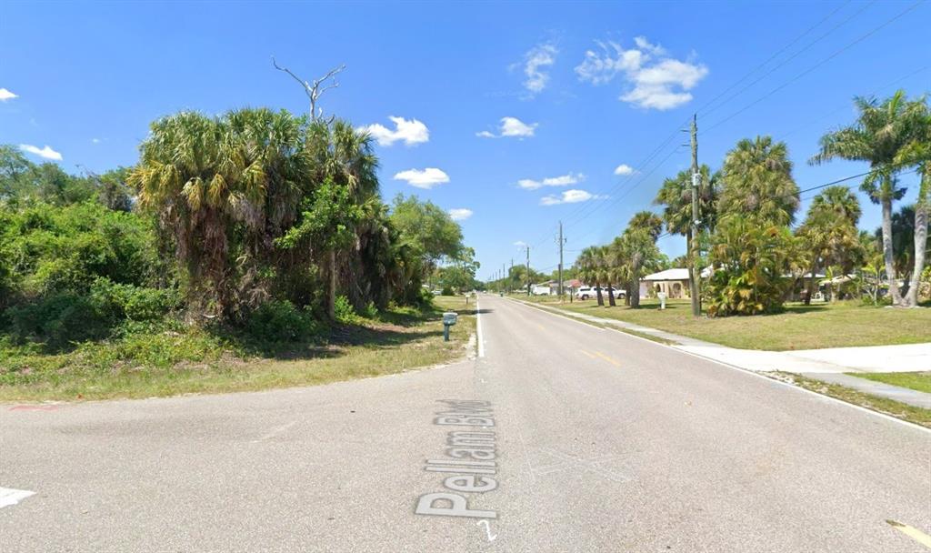 A paved street stretches into the distance, flanked by lush trees and residential properties — 18504 YARBROUGH AVENUE, PORT CHARLOTTE, FL