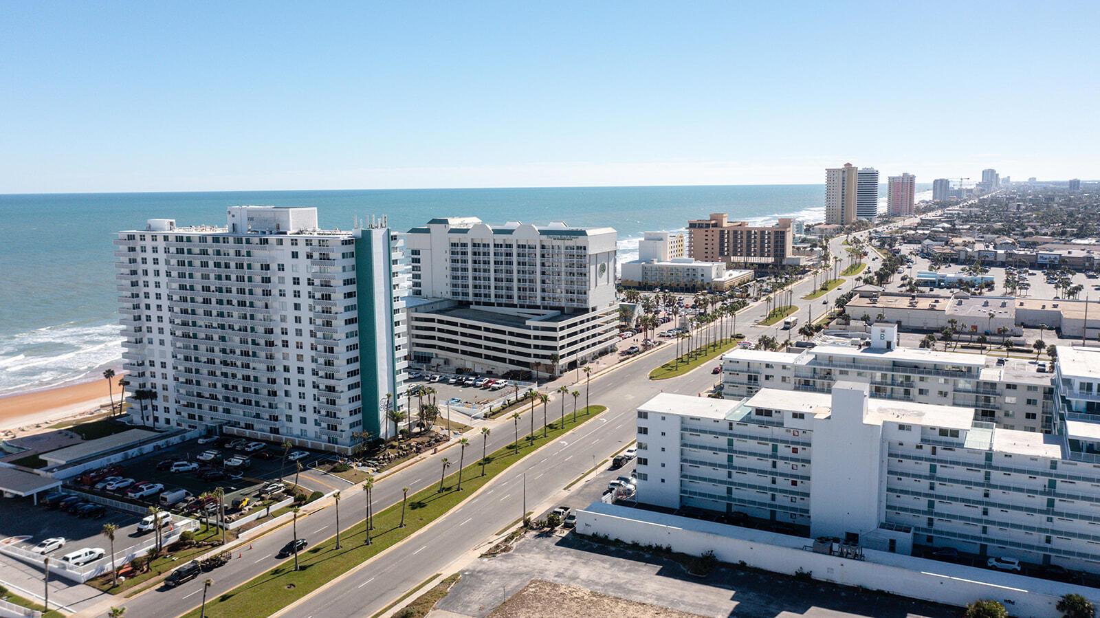 An aerial view shows high-rise hotels and condominiums along a beach road near the ocean — 2800 N Atlantic Avenue Unit 712, FL 32118, FL