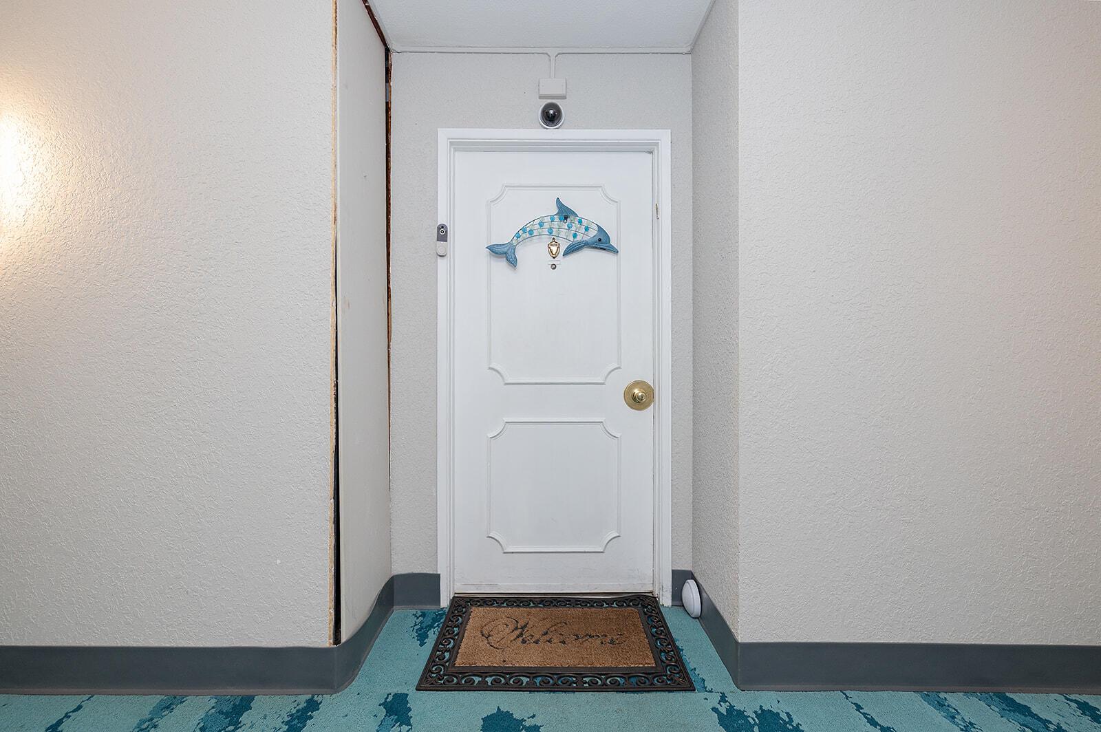 A white door with a dolphin decoration and a welcome mat in a hallway — 2800 N Atlantic Avenue Unit 712, FL 32118, FL
