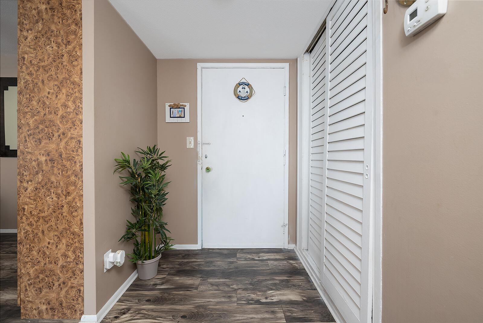 An entryway features a white door, wood-look flooring, a potted plant, and louvered closet doors — 2800 N Atlantic Avenue Unit 712, FL 32118, FL