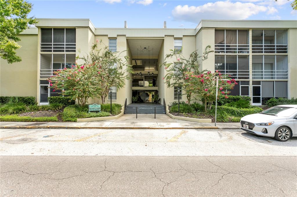 A three-story apartment building with a central entrance, screened balconies, and a parked white car — 2302 S MANHATTAN AVENUE UNIT 111, TAMPA, FL