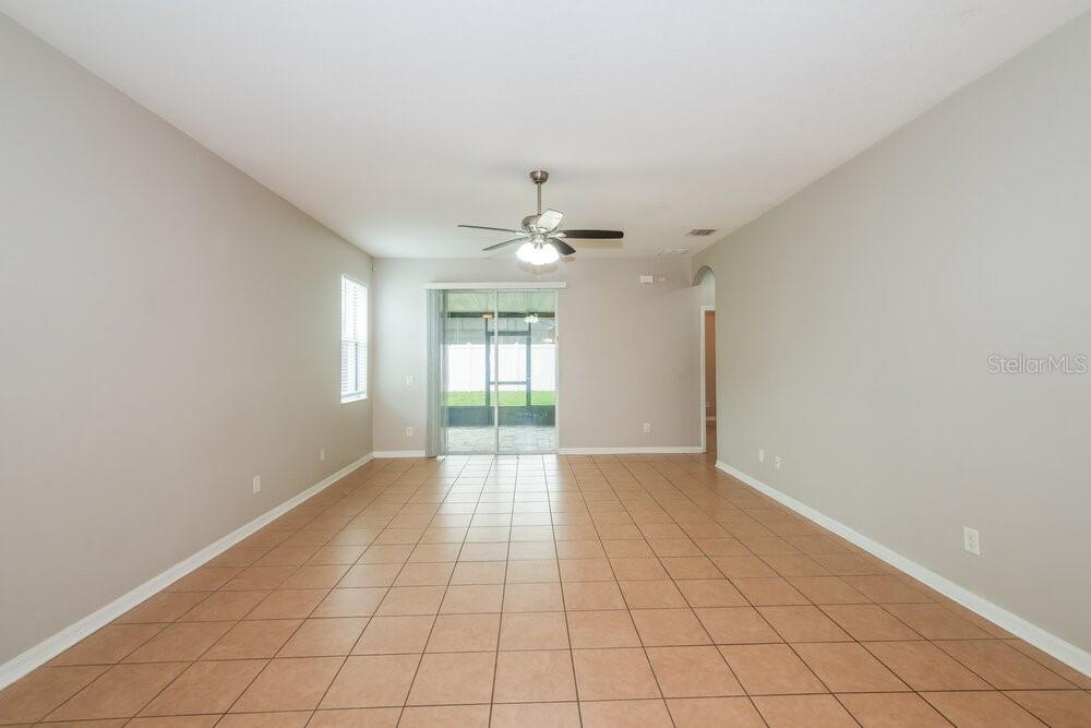 An empty living room features light-colored walls, tile flooring, a ceiling fan, and sliding doors — 8226 SUMMER WOOD LANE, RIVERVIEW, FL