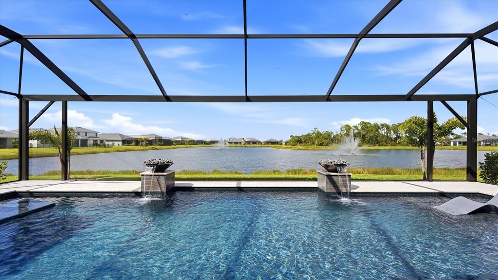 A swimming pool with two water features overlooks a lake under a screened enclosure — 12866 PINNACLE LANE, VENICE, FL