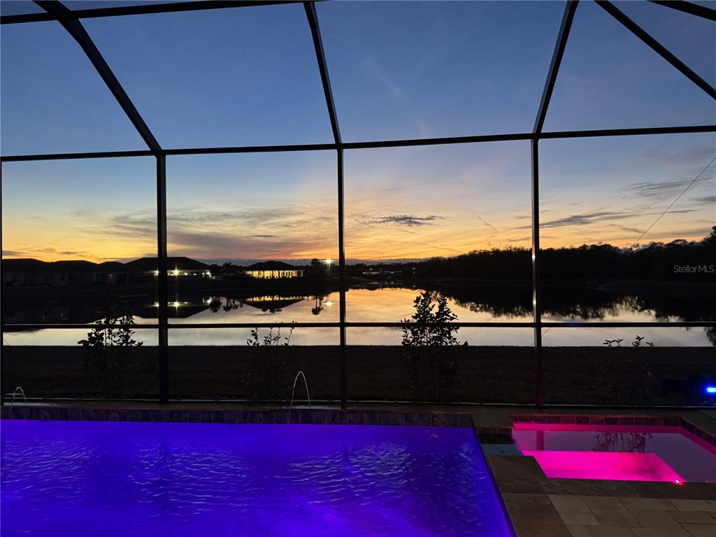 A swimming pool with purple lighting overlooks a lake at sunset from a screened lanai — 13060 WILLOW GROVE DRIVE, RIVERVIEW, FL