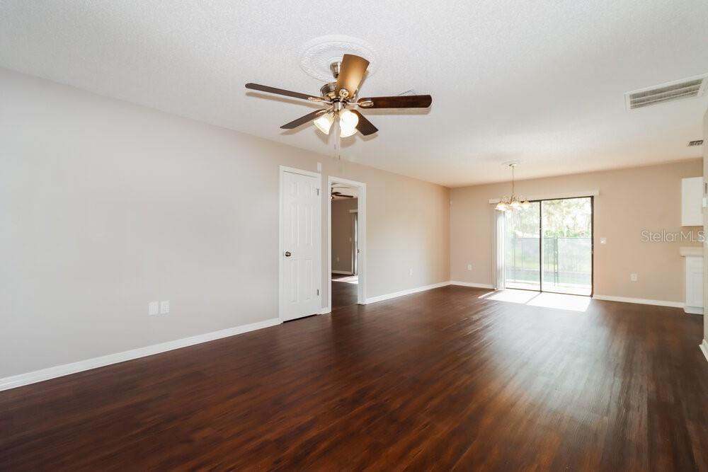 An empty living room with dark wood-look flooring, a ceiling fan, and sliding glass doors — 10564 BLYTHVILLE ROAD, SPRING HILL, FL