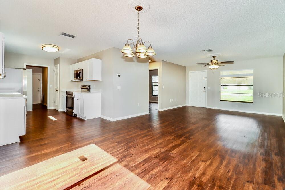 An open-concept kitchen and living area featuring white cabinets, dark wood flooring, and a chandelier — 10564 BLYTHVILLE ROAD, SPRING HILL, FL