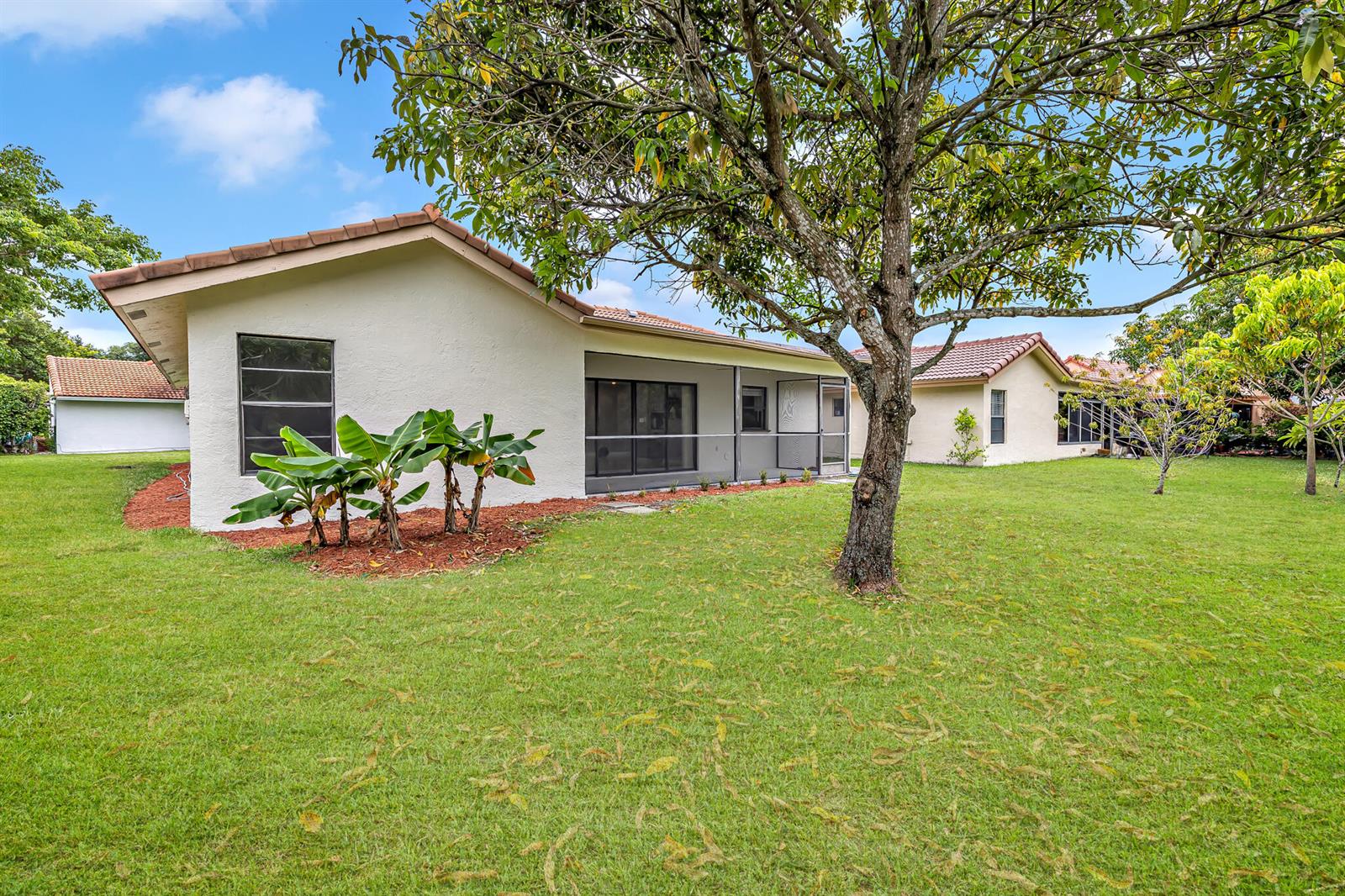 A backyard view of a single-story house with a screened patio and a large tree — 1273 Spring Circle Drive, Coral Springs FL 33071, CORAL SPRINGS, FL