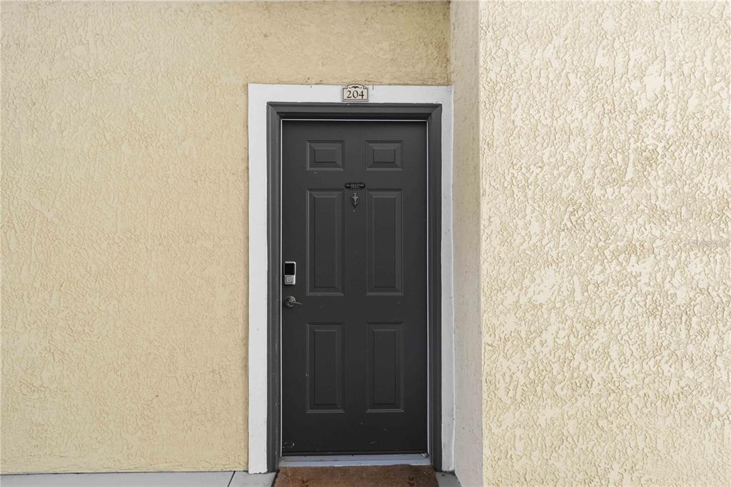 A dark gray front door with a number 204 plaque sits in a textured wall — 10201 COURTNEY PALMS BOULEVARD UNIT 204, TAMPA, FL