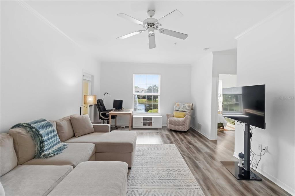 A living room features a sectional sofa, a desk, a television, and a window view — 10201 COURTNEY PALMS BOULEVARD UNIT 204, TAMPA, FL