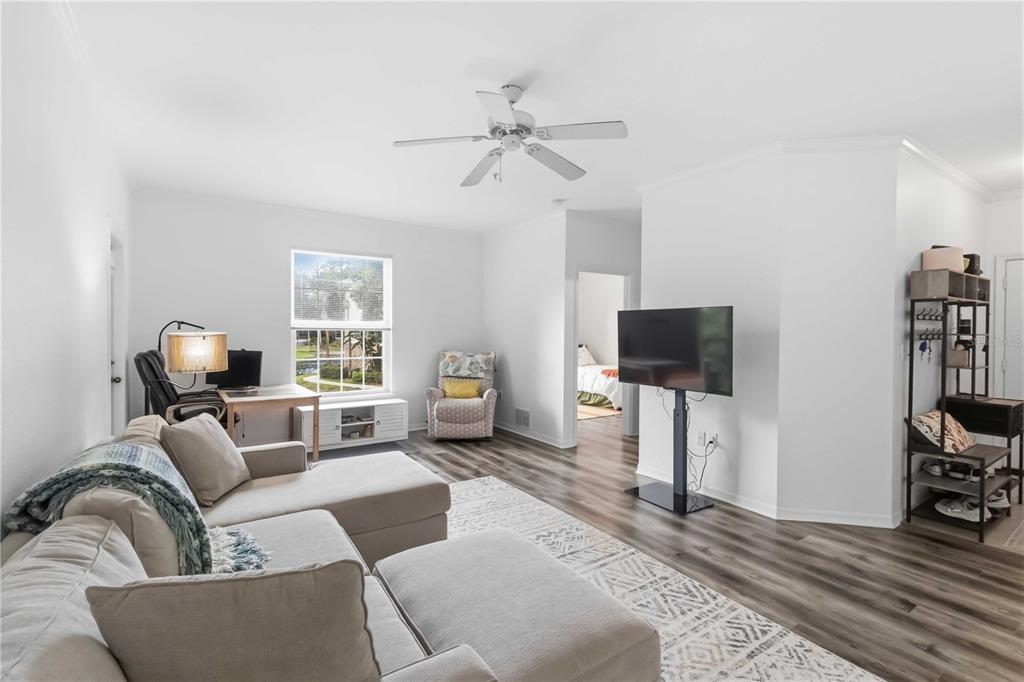 A living room features a sectional sofa, a television on a stand, and wood-look flooring — 10201 COURTNEY PALMS BOULEVARD UNIT 204, TAMPA, FL