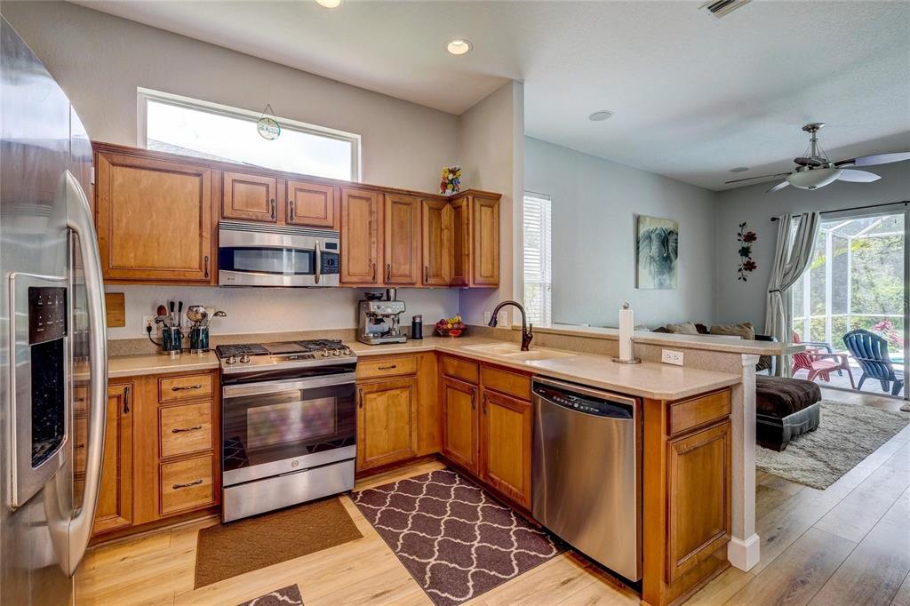 A kitchen with wood cabinets, stainless steel appliances, and a breakfast bar overlooking a living area — 6462 GOLDEN LEAF COURT, LAKEWOOD RANCH, FL