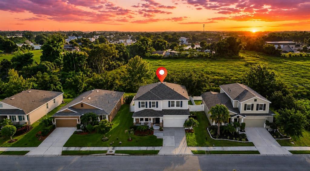An aerial view shows three suburban houses at sunset with a red location pin above — 6116 35TH COURT E, BRADENTON, FL