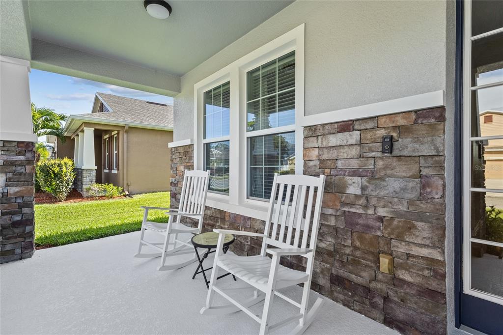 A covered front porch features two white rocking chairs, stone siding, and a glass door — 6116 35TH COURT E, BRADENTON, FL