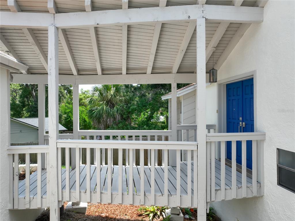 A covered wooden deck with white railings leads to a bright blue double door — 1215 DUNCAN COURT, LONGWOOD, FL