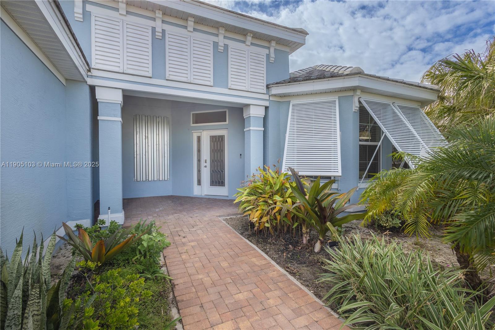 The exterior of a light blue house features a brick walkway and white hurricane shutters — 2547 Saint Lucia Cir, Vero Beach FL 32967, VERO BEACH, FL