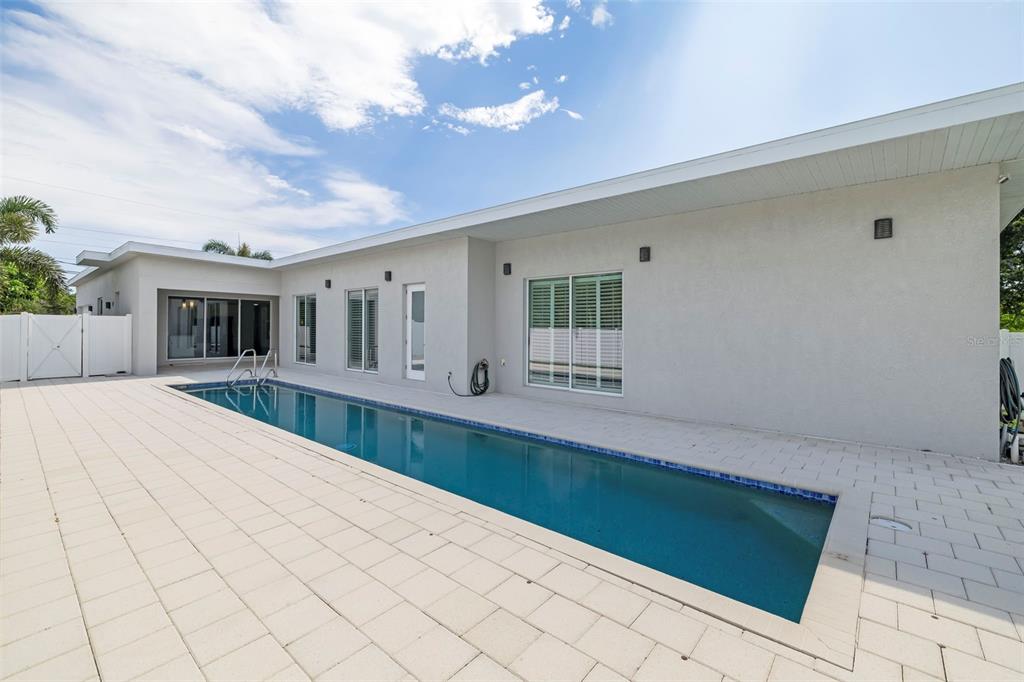 A long rectangular swimming pool sits on a paved patio beside a modern white house — 4524 RIVERWOOD AVENUE, SARASOTA, FL