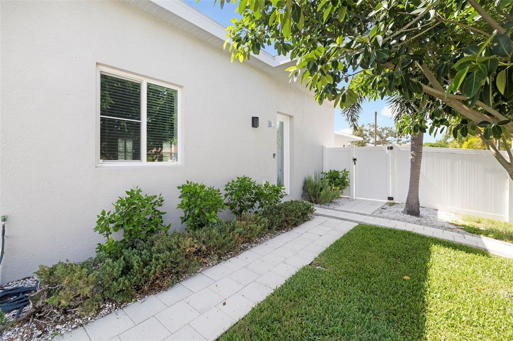 A paved walkway leads to a white house exterior with a window and landscaping — 4524 RIVERWOOD AVENUE, SARASOTA, FL