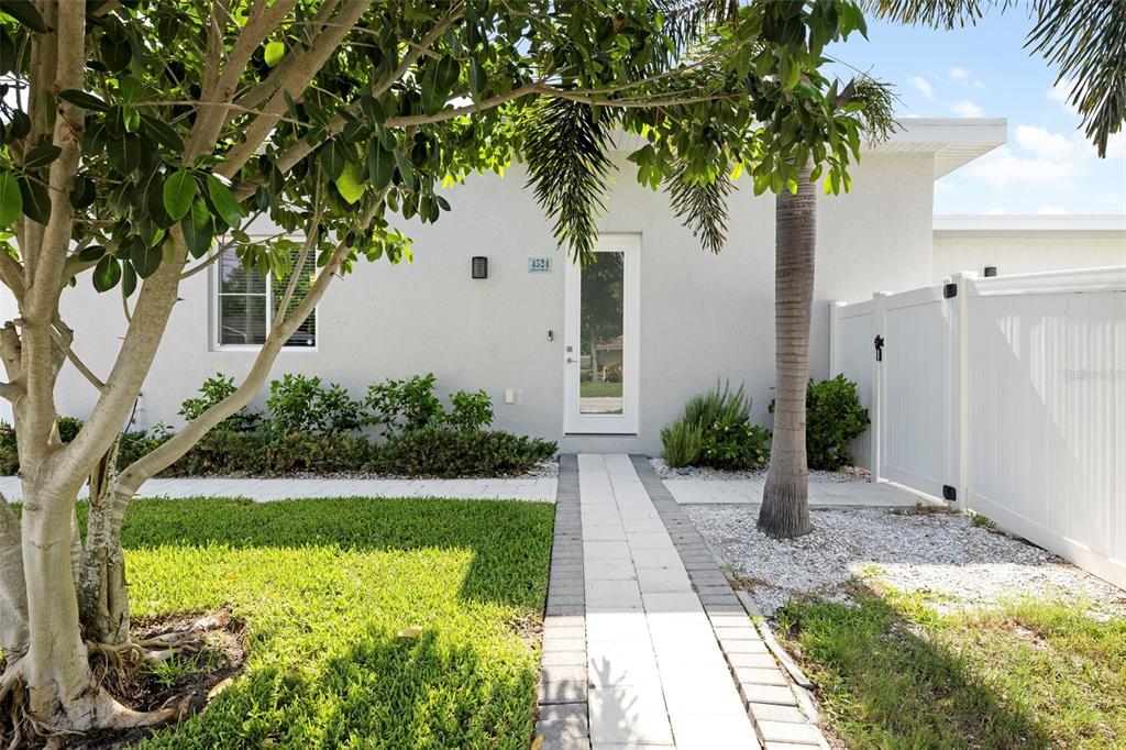 A paved walkway leads to the front entrance of a light-colored house with landscaping — 4524 RIVERWOOD AVENUE, SARASOTA, FL