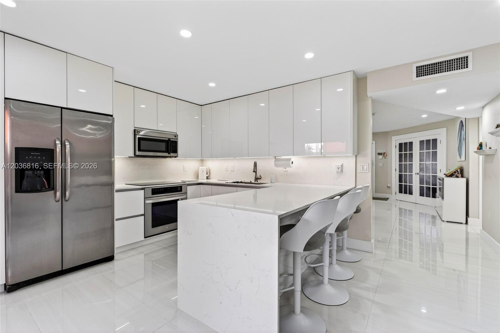 A modern kitchen features white glossy cabinets, a stainless steel refrigerator, and a marble-topped island — 11115 W Okeechobee Rd # 123, Hialeah Gardens FL 33018, HIALEAH GARDENS, FL
