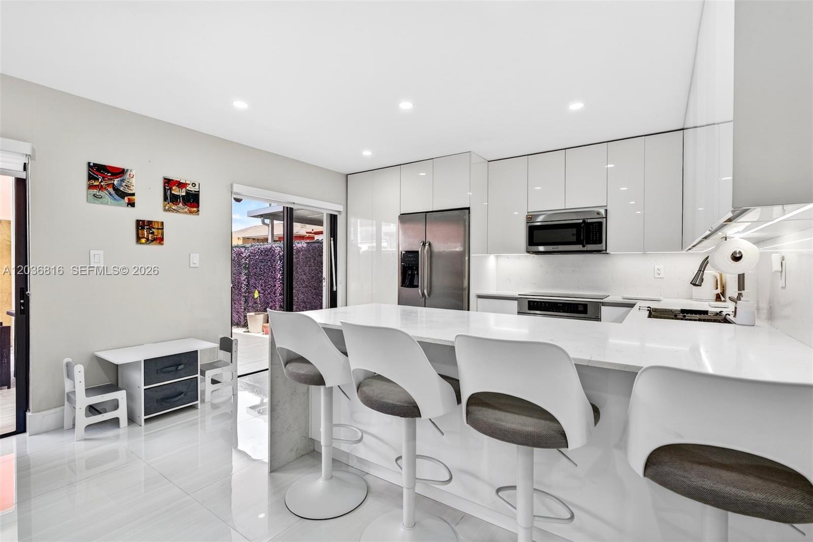 A modern kitchen features white glossy cabinets, a quartz island with bar stools, and tile flooring — 11115 W Okeechobee Rd # 123, Hialeah Gardens FL 33018, HIALEAH GARDENS, FL