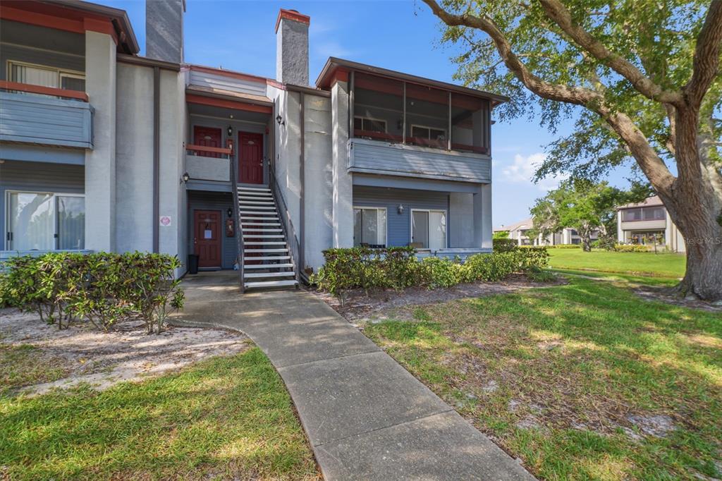 A two-story apartment building features a concrete walkway leading to an exterior staircase and balconies — 10263 GANDY BOULEVARD N UNIT 408, ST PETERSBURG, FL