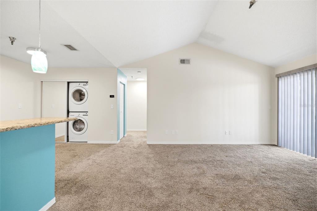 A living room with beige carpet, vaulted ceilings, a turquoise kitchen island, and stacked laundry machines — 10263 GANDY BOULEVARD N UNIT 408, ST PETERSBURG, FL