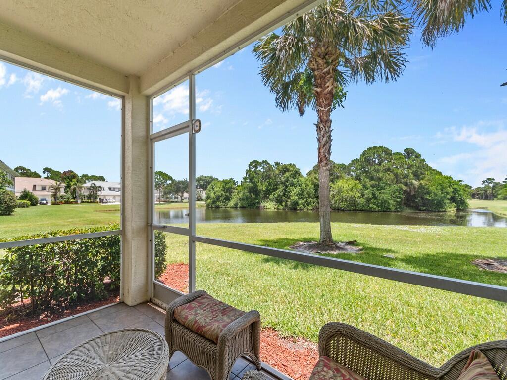 A screened-in patio with wicker furniture overlooks a grassy lawn, a pond, and palm trees — 4210 Gator Trace Avenue # B, Fort Pierce FL 34982, FORT PIERCE, FL