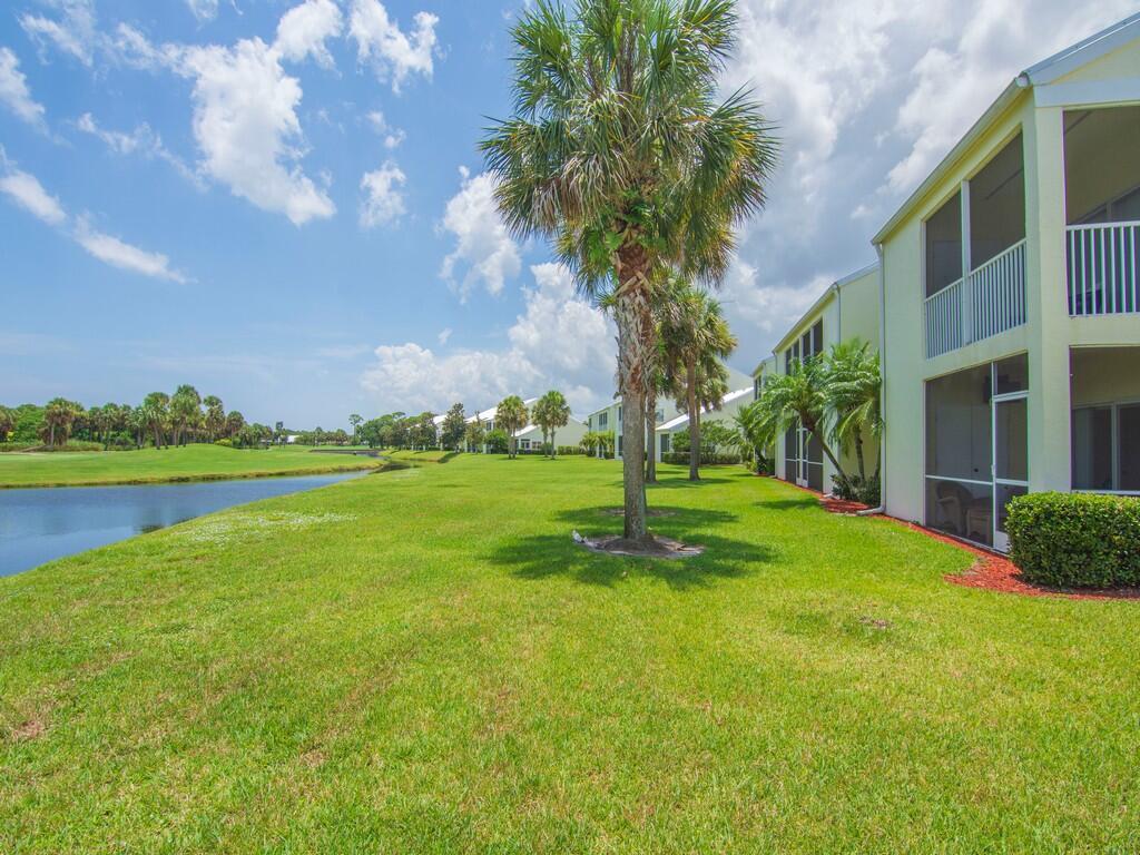 A view of a multi-story apartment building exterior with a lawn, pond, and palm trees — 4210 Gator Trace Avenue # B, Fort Pierce FL 34982, FORT PIERCE, FL