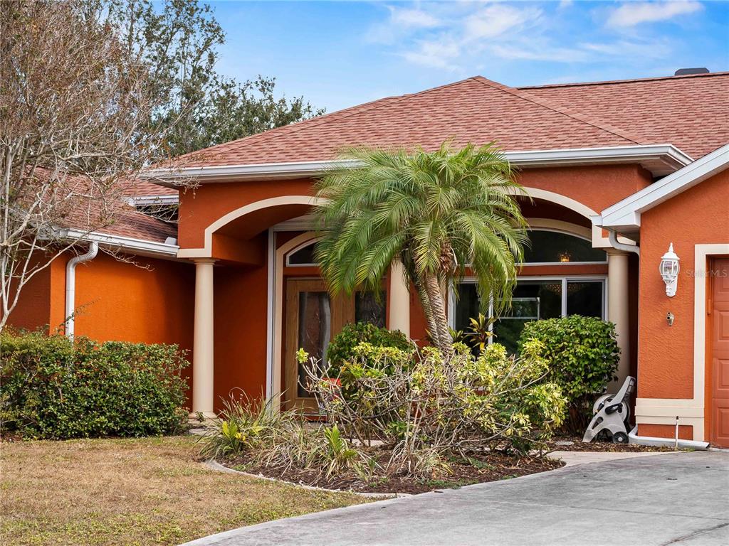 The exterior of a house features orange stucco walls, a palm tree, and a covered entryway — 1794 OKETO STREET, NORTH PORT, FL