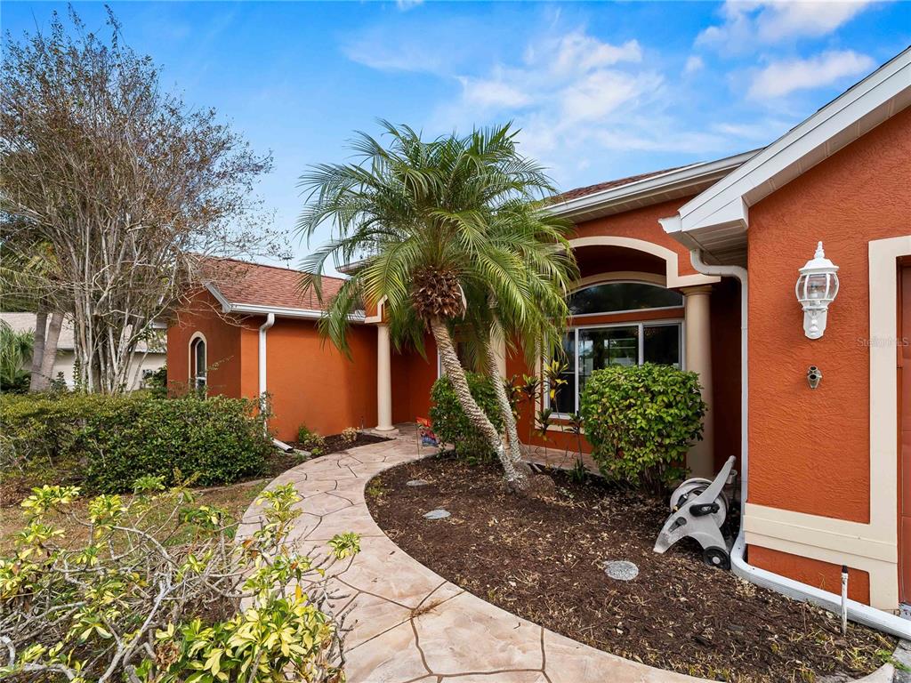 A curved stone walkway leads to the entrance of a house with orange stucco walls — 1794 OKETO STREET, NORTH PORT, FL