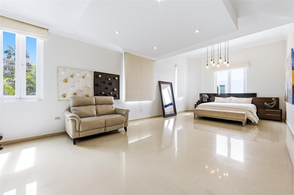 A spacious bedroom features a beige sofa, a king-sized bed, and polished light-colored tile floors — 8WMH+P23 LAS FLORES DE MONTEHIEDRA, SAN JUAN, PR