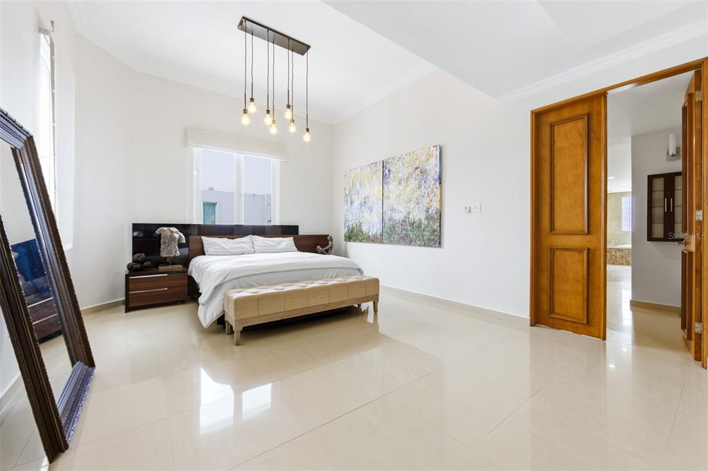 A bedroom features a bed with a bench, a large mirror, and a hanging light fixture — 8WMH+P23 LAS FLORES DE MONTEHIEDRA, SAN JUAN, PR