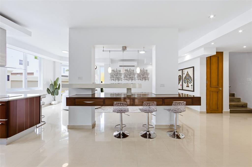 A modern kitchen features a wooden breakfast bar with three transparent stools and white walls — 8WMH+P23 LAS FLORES DE MONTEHIEDRA, SAN JUAN, PR