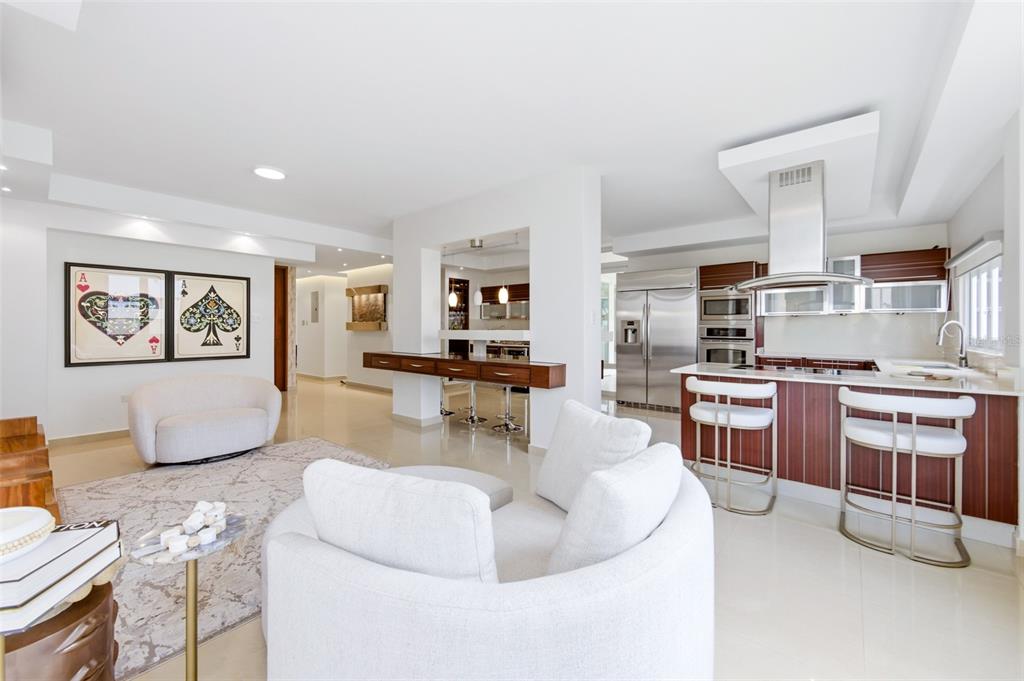 A modern open-concept living room and kitchen with white furniture, tile floors, and wood cabinetry — 8WMH+P23 LAS FLORES DE MONTEHIEDRA, SAN JUAN, PR
