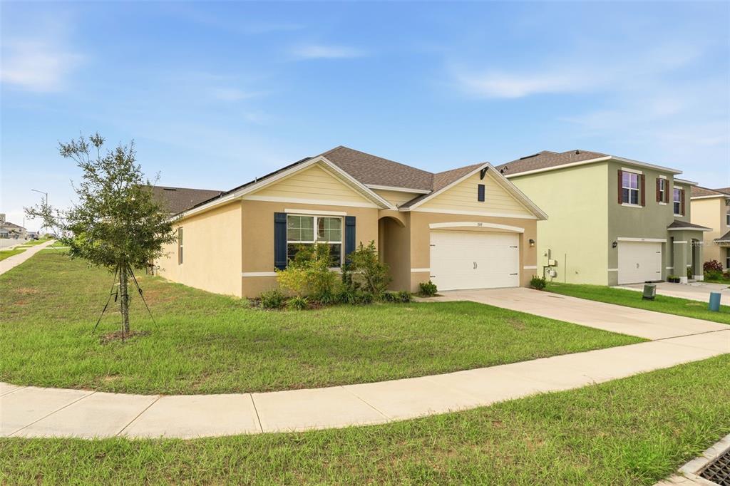 A tan single-story house with a two-car garage and a green lawn — 1349 SUGARWOOD STREET, DAVENPORT, FL